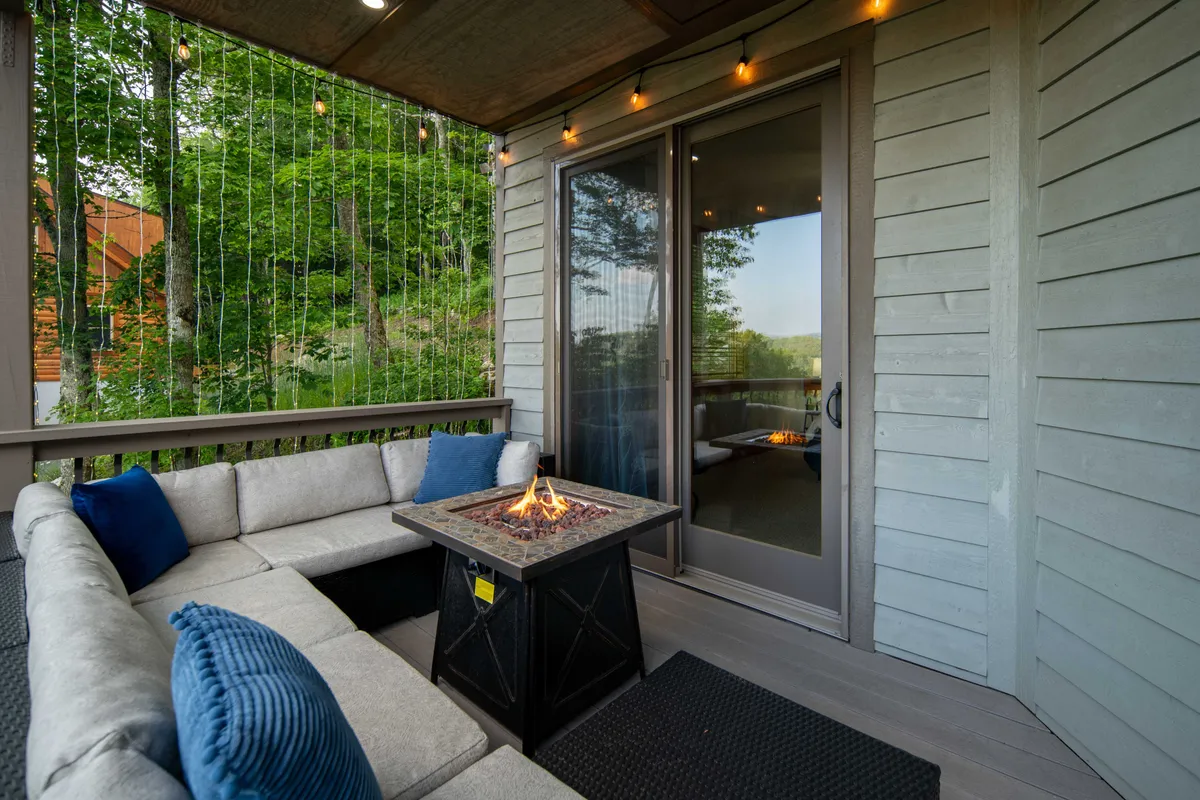 A cozy outdoor fire pit area with seating and string lights, adjacent to a sliding glass door leading inside. The setup is inviting for evening relaxation and socializing after a day outdoors, with enough space for pets to linger and enjoy the atmosphere.