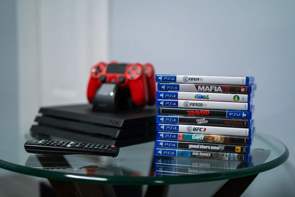 A close-up of the PS4 console with a red controller, a stack of video games, and a remote, set on a shelf or table. The setup suggests hours of immersive play and entertainment for guests of all ages.