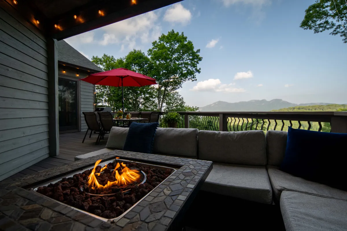 An inviting fire pit with comfortable seating and an umbrella set against a dramatic mountain backdrop. The scene suggests a cozy gathering spot for unwinding or sharing stories after time on the trails.