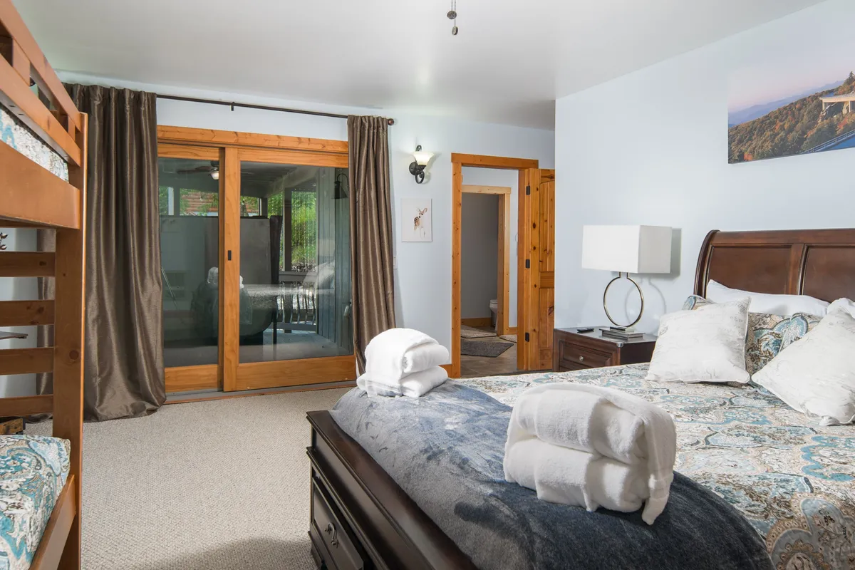 A bright, comforting bedroom with a king-size bed and twin-over-twin bunk beds, highlighted by sliding glass doors and decorative artwork. The space encourages relaxation and family bonding, with sunlight streaming in and a layout that invites both solo and group stays.