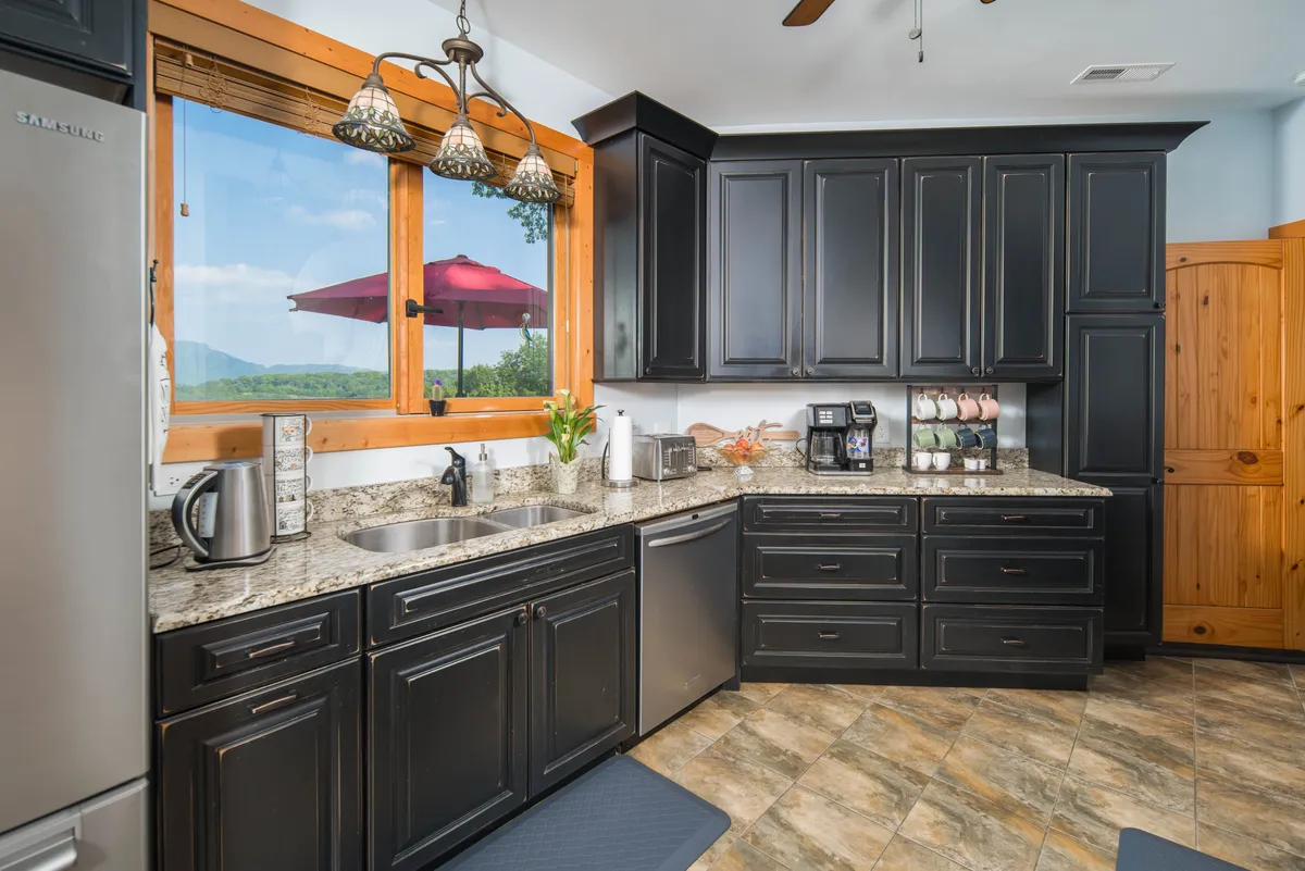 A well-equipped kitchen with granite countertops, black cabinetry, modern appliances, and a large window offering scenic views. The kitchen island is ready for preparing group feasts or casual morning coffees, and the space feels both functional and inviting.