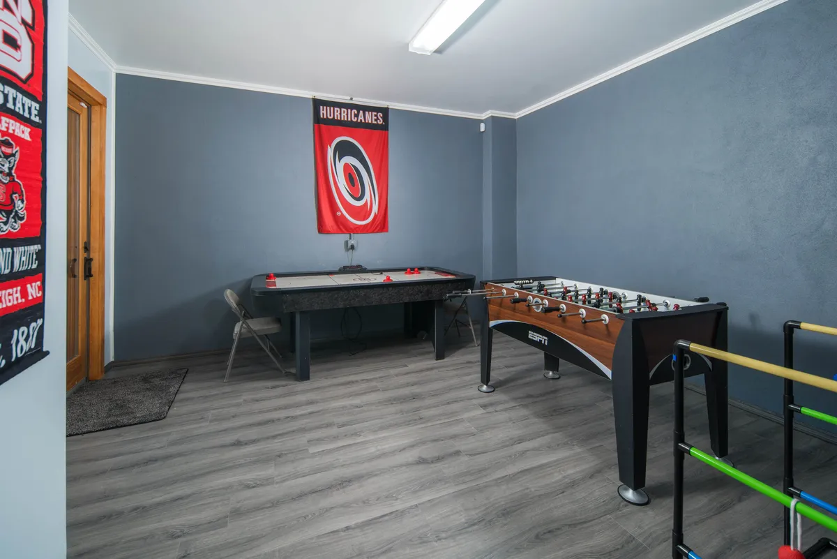 An energetic indoor recreation room with a foosball table, air hockey table, and team banner. The space has a lively mood, suggesting fun group activities and family-friendly entertainment after outdoor adventures.