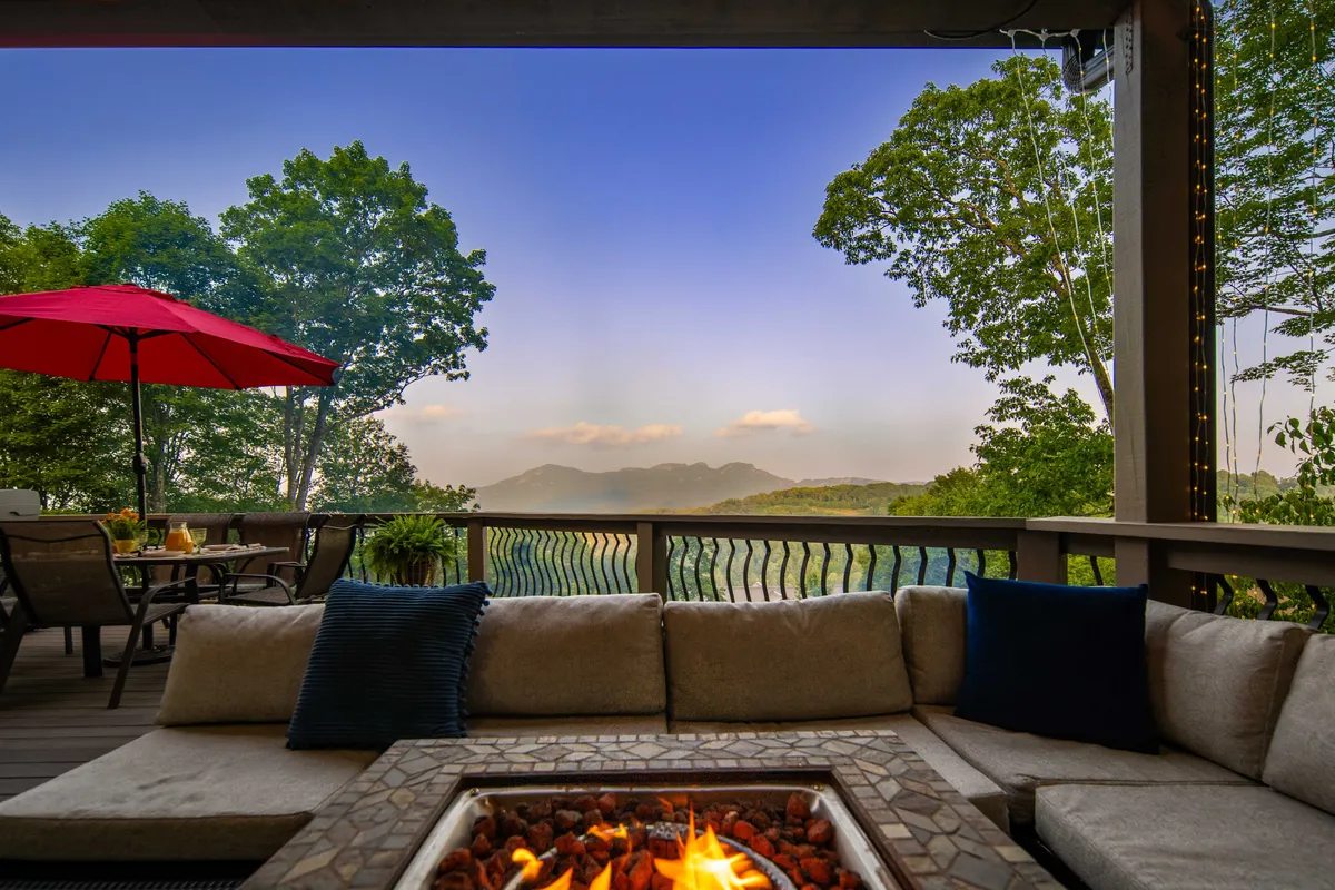 This exterior image highlights a cozy fire pit surrounded by seating, all set against a panoramic mountain view and anchored by a striking red umbrella. Twilight lighting enhances the mood of relaxation and camaraderie, suggesting a perfect spot for après-ski gatherings, warm drinks, and storytelling as the sun sets over the mountains.