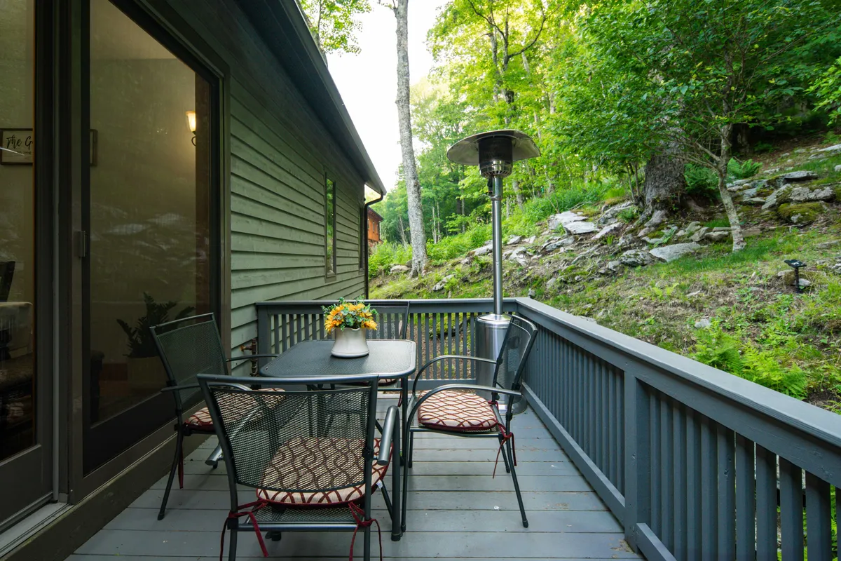 A serene patio setting with a dining table, chairs, flower centerpiece, and patio heater. The space is designed for outdoor dining, relaxation, and entertaining while enjoying the surrounding nature.
