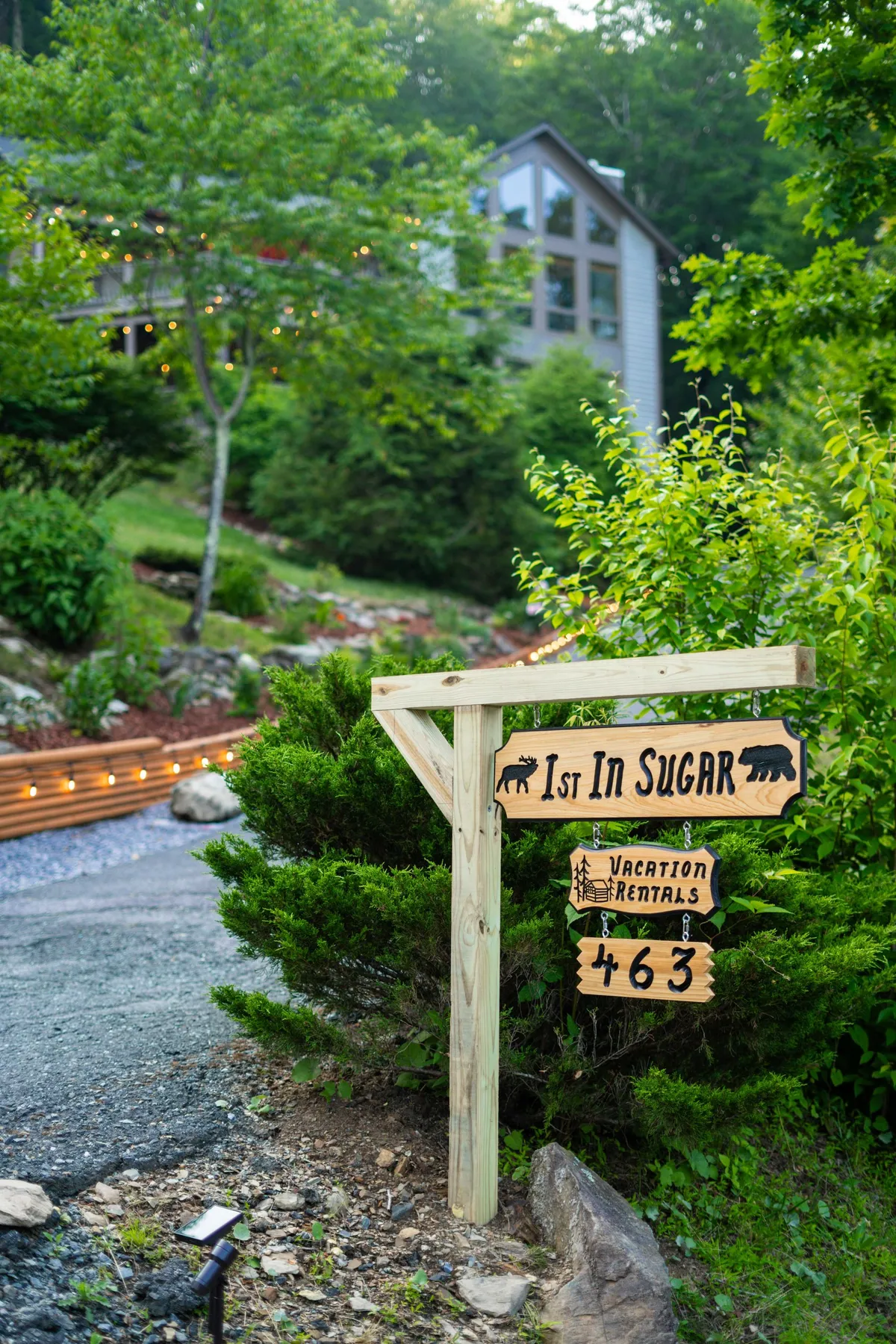 An inviting exterior view featuring a wooden '1st In Sugar' sign, natural greenery, and an illuminated pathway. The setting is cozy yet adventurous, signaling the beginning of memorable family gatherings and exploration.
