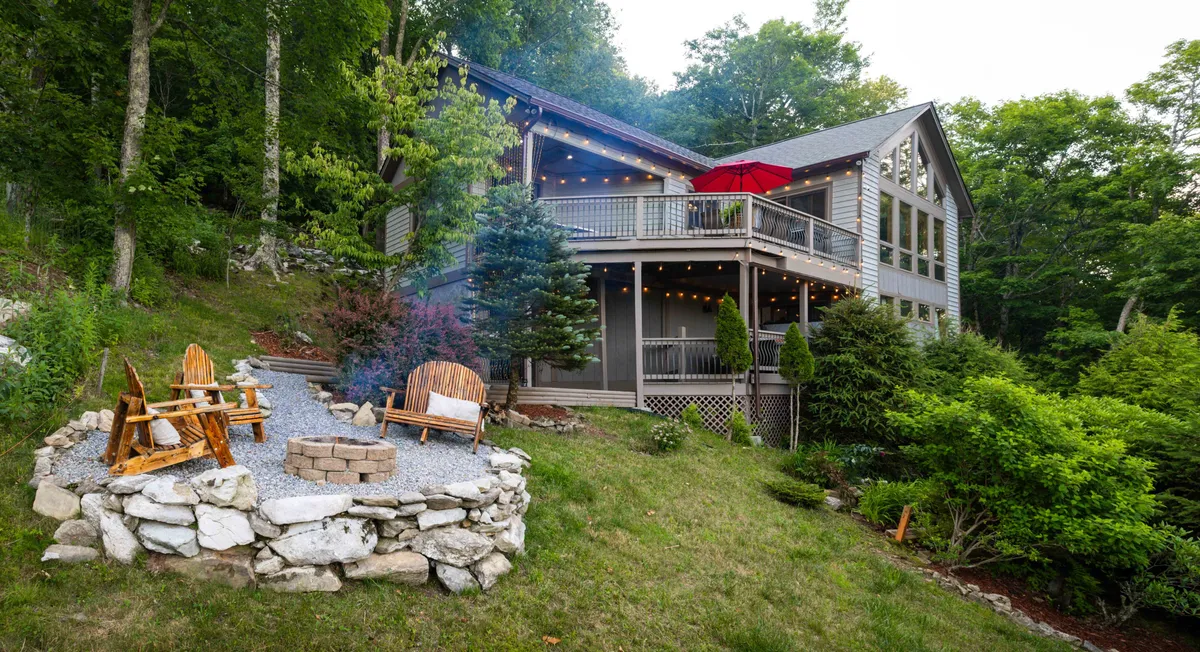This exterior image showcases the house with a fire pit surrounded by Adirondack chairs, all set against a backdrop of trees. The scene invites groups to gather outdoors, enjoy storytelling, roast marshmallows, and take in the natural surroundings, reinforcing the idea of communal bonding in nature.