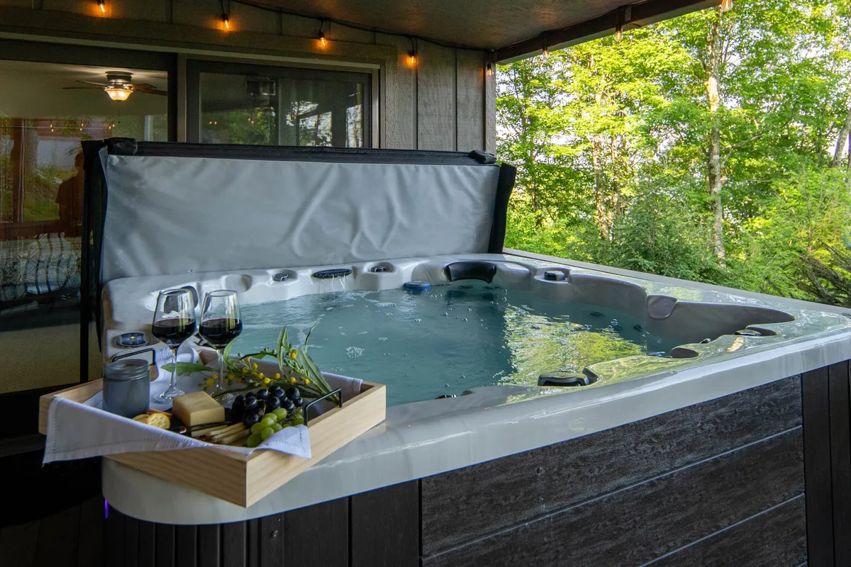 A tranquil exterior shot featuring a private hot tub nestled among greenery, with a charcuterie board and glasses of wine set close by. The inviting setup highlights relaxation and socializing, with hints of sunset lighting to create a cozy ambiance.