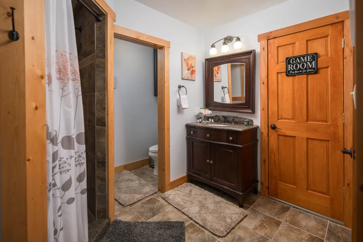 A bathroom adjacent to the playroom, featuring a vanity with mirror, a door leading to the game room, and a visible shower curtain. The space feels convenient and accessible—ideal for quick clean-ups after active play or outdoor activities.