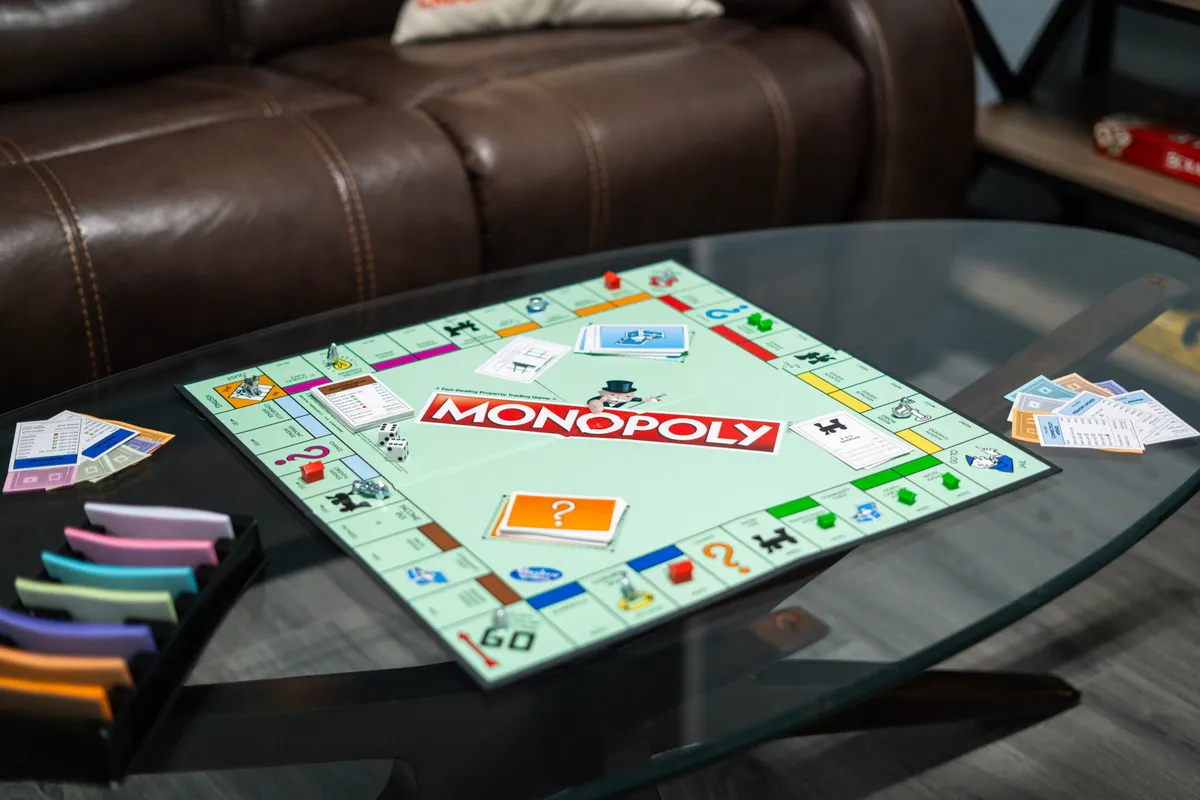 This close-up interior image features a Monopoly board with dice, colored tokens, and play money, set up for a game night. The table scene is lively and evokes nostalgia, highlighting a classic family bonding activity.