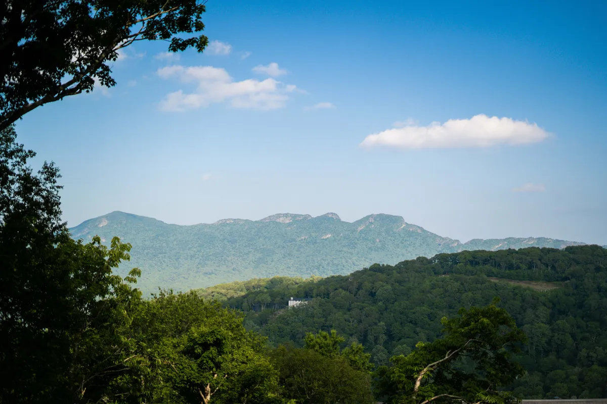 A sweeping view of mountains, clouds, and trees, inviting thoughts of hiking, exploration, and taking in panoramic vistas. The untouched landscape ties directly to local outdoor adventure opportunities.