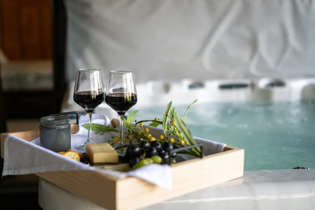 A serene hot tub scene featuring two wine glasses, a wooden tray with snacks, and a bubbling spa. The atmosphere is tranquil and romantic, indicating a restorative soak after a day on the slopes.